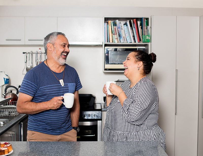 A father and daughter share a laugh and a hot drink in the kitchen.