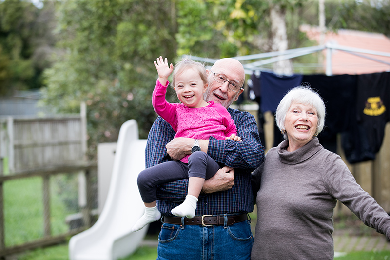 Grandparents play with their granddaughter who is waving at the camera.